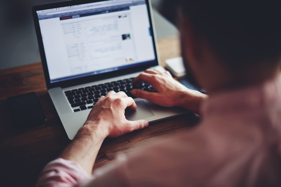 Cropped image of a young male student texting on computer sittin