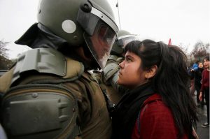 a young girl and a soldier dressed in riot gear stare one another down during a protest in Santiago, Chile. The protest decried the 1973 coup that deposed the elected president and led to a 17 year vicious reign by the Chilean military.