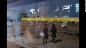 Soldiers are seen in the reflection from a bus window carrying children and other civilians out of a suburb of Damascus, Syria. The warring forces in the six year old civil war that has murdered thousands, agreed to allow people to escape the suburb so that the murder could resume between the warring factions' soldiers.